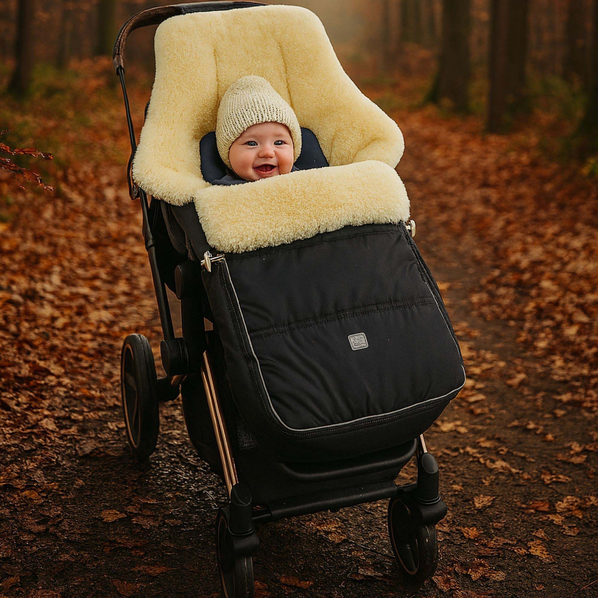 Baby sitzt im Lammfellfußsack im Kinderwagen auf verschneitem Waldweg, warm eingekuschelt