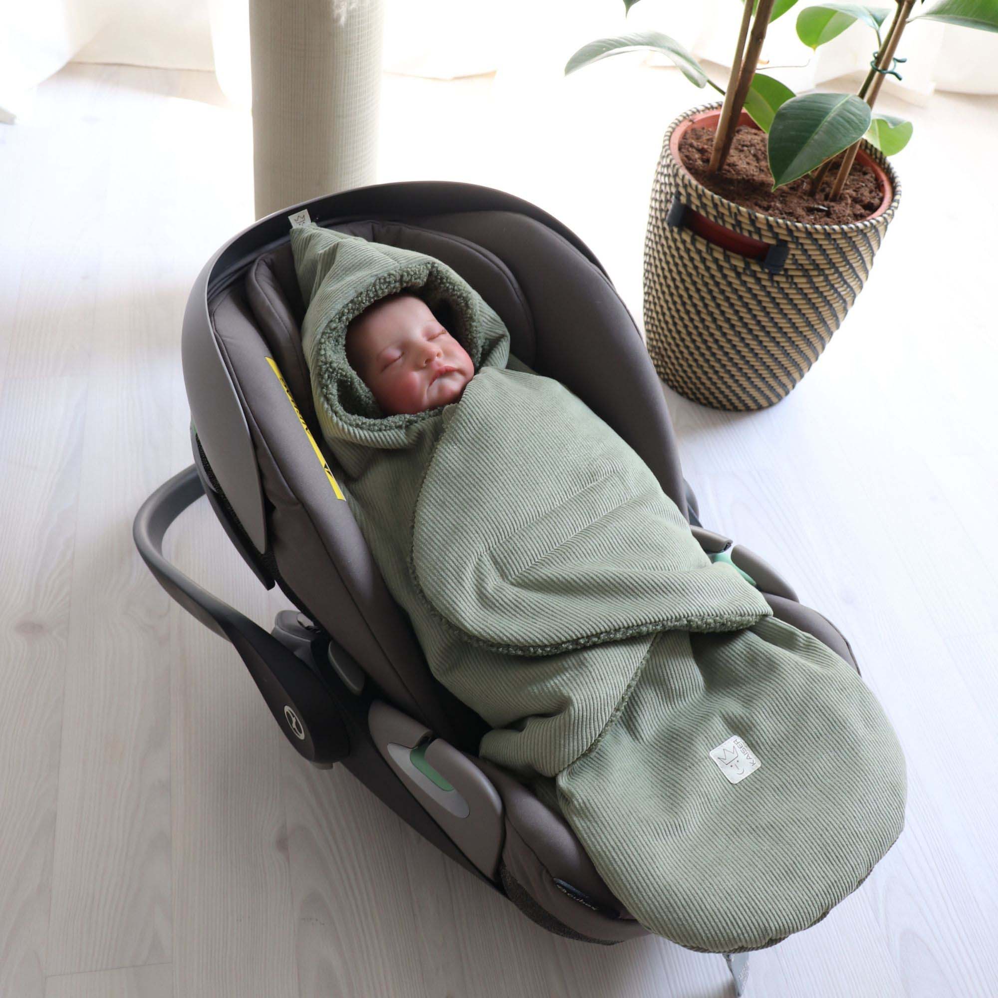 Baby liegt eingepackt im braunen Fußsack in einer Babyschale – Szene in heller Wohnumgebung.
