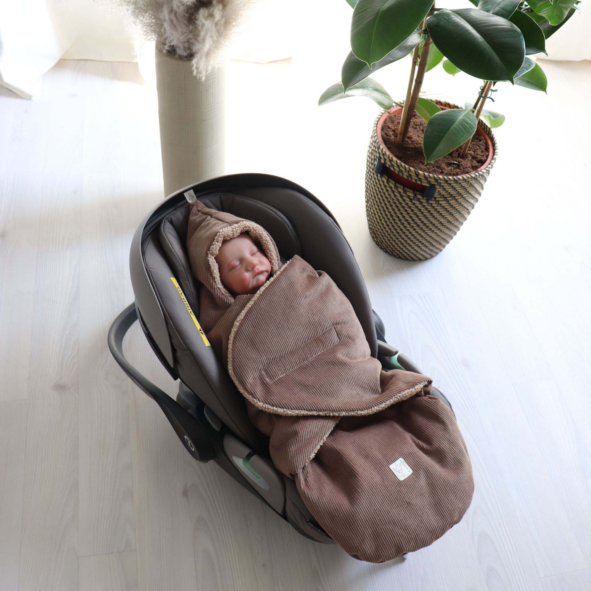 Baby liegt eingepackt im braunen Fußsack in einer Babyschale – Szene in heller Wohnumgebung.