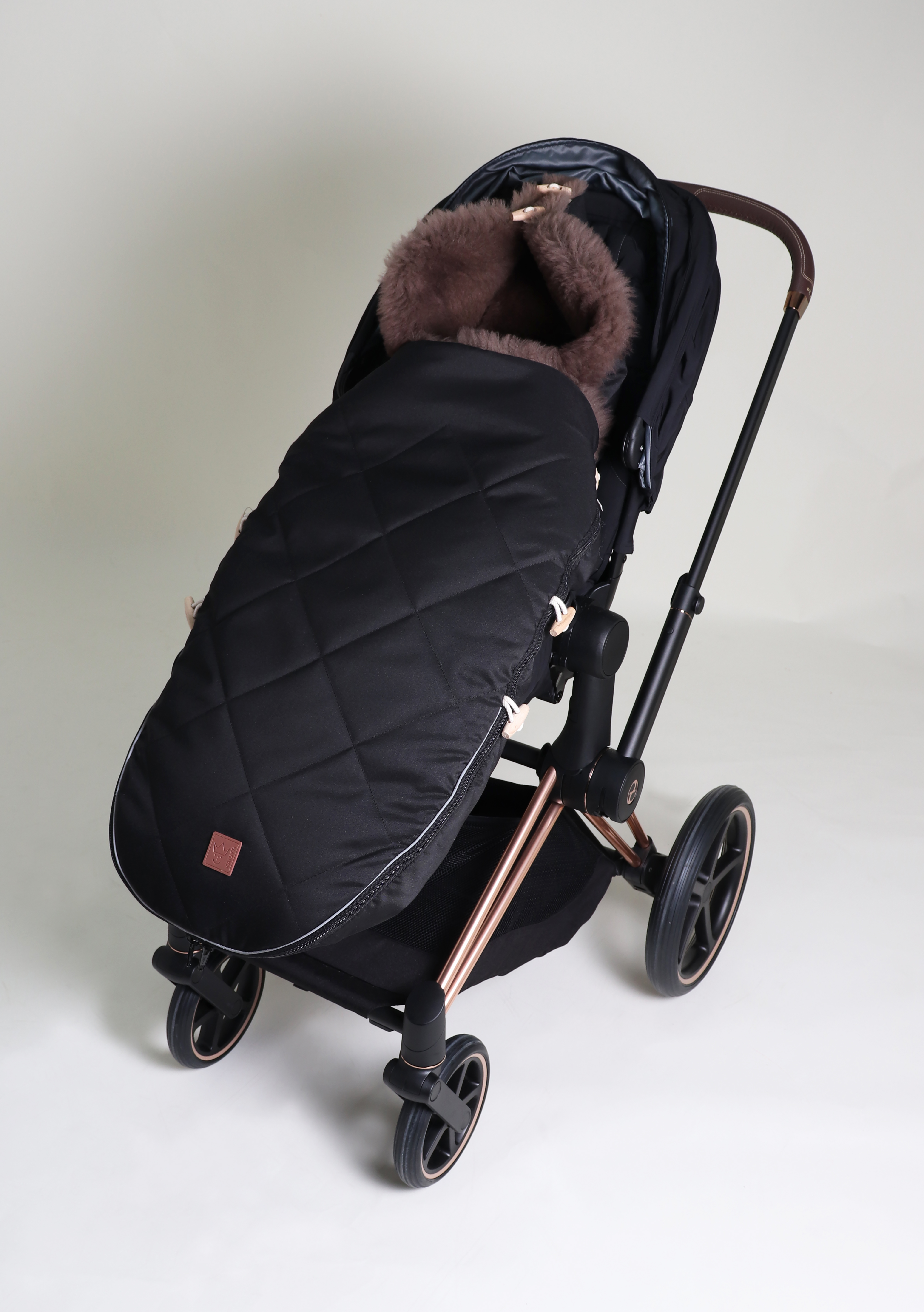 Fußsack mit beigem Lammfell-Innenfutter in der Farbe black ist in einem Kinderwagen eingesetzt