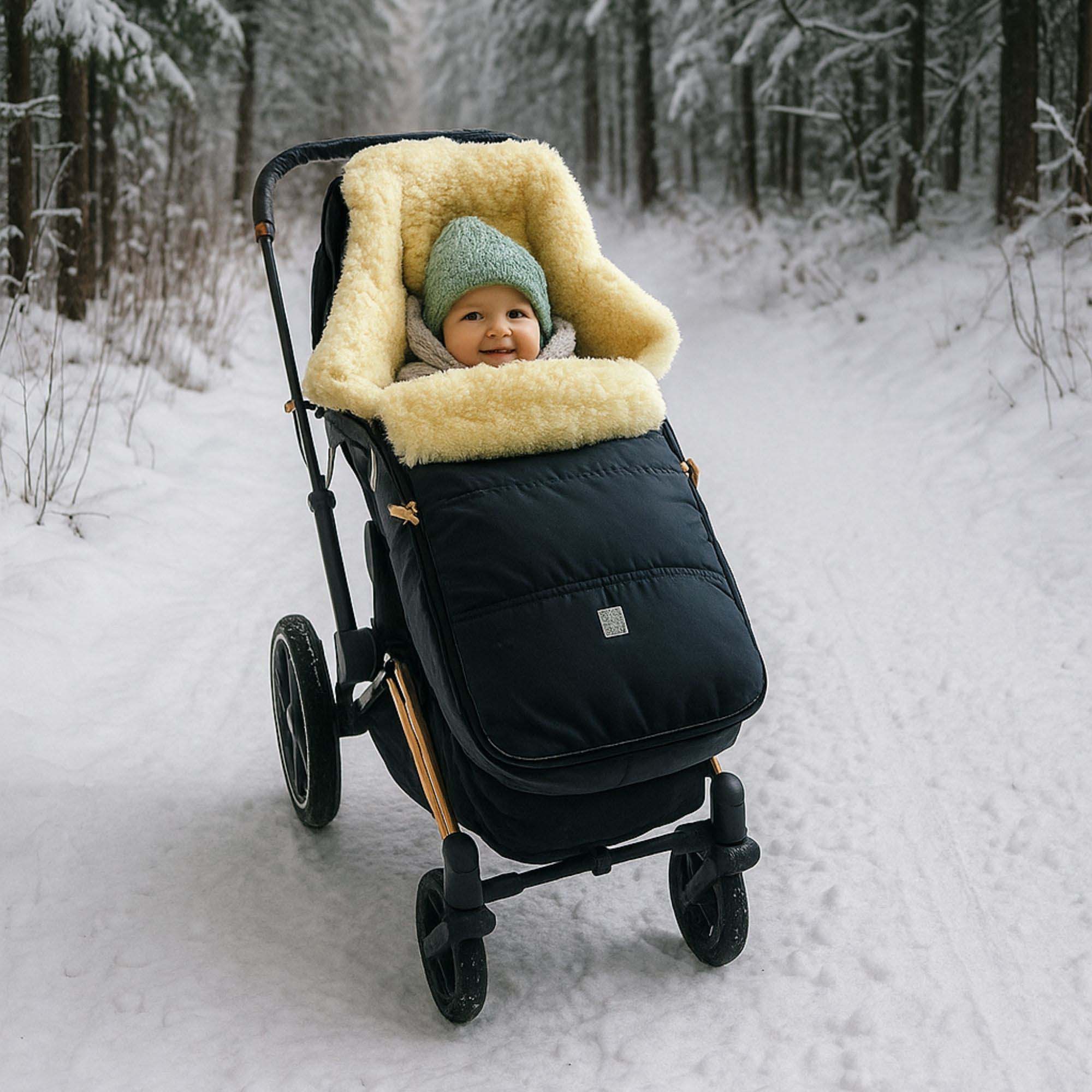 Baby sitzt im Lammfellfußsack im Kinderwagen auf verschneitem Waldweg, warm eingekuschelt