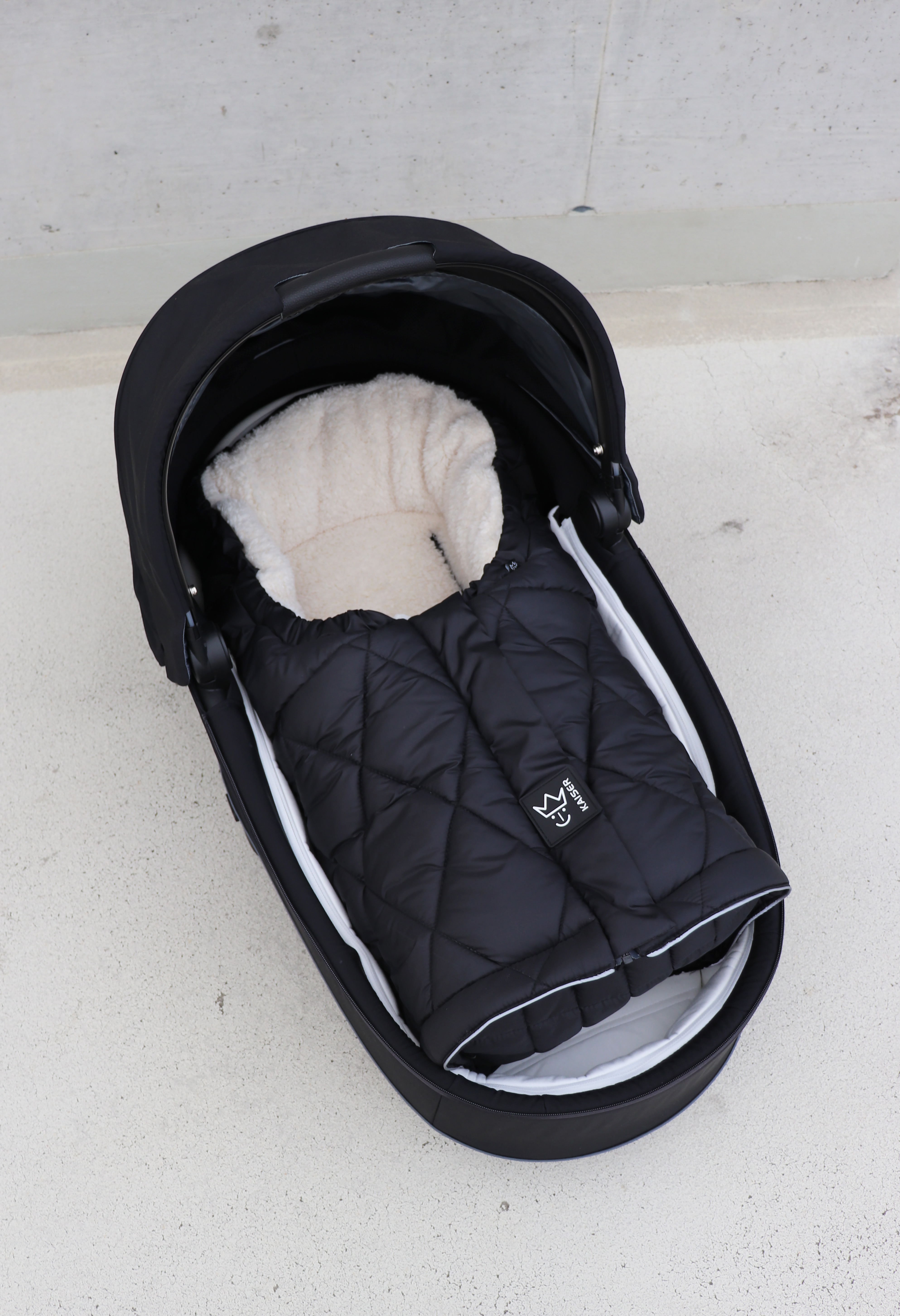 Geschlossener Fußsack mit einem Sherpa-Futter in der Farbe schwarz/creme liegt in einer Babyschale