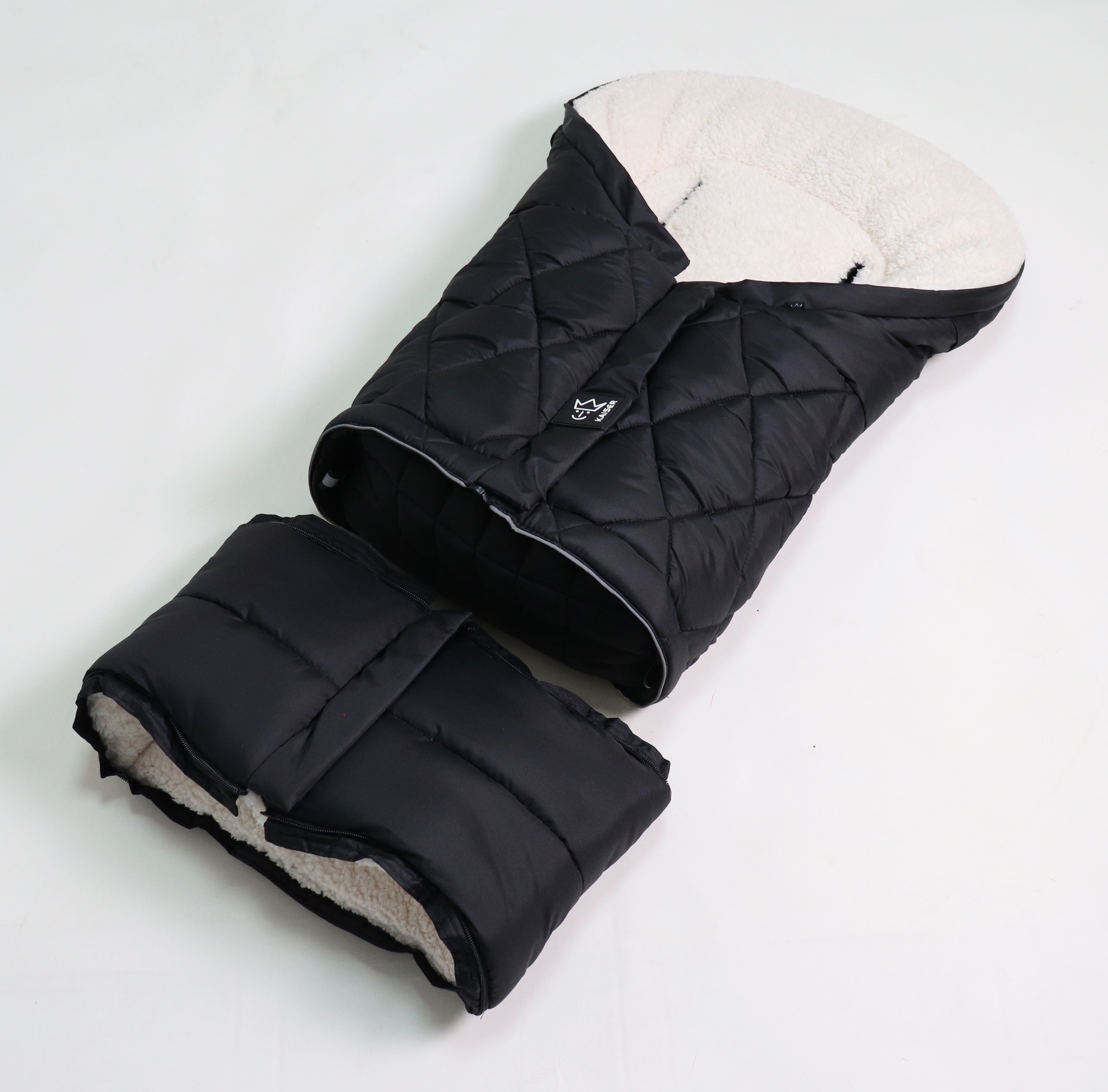 Fußsack mit einem Sherpa-Futter in der Farbe schwarz/creme und gestepptem Design, geöffnet dargestellt.
