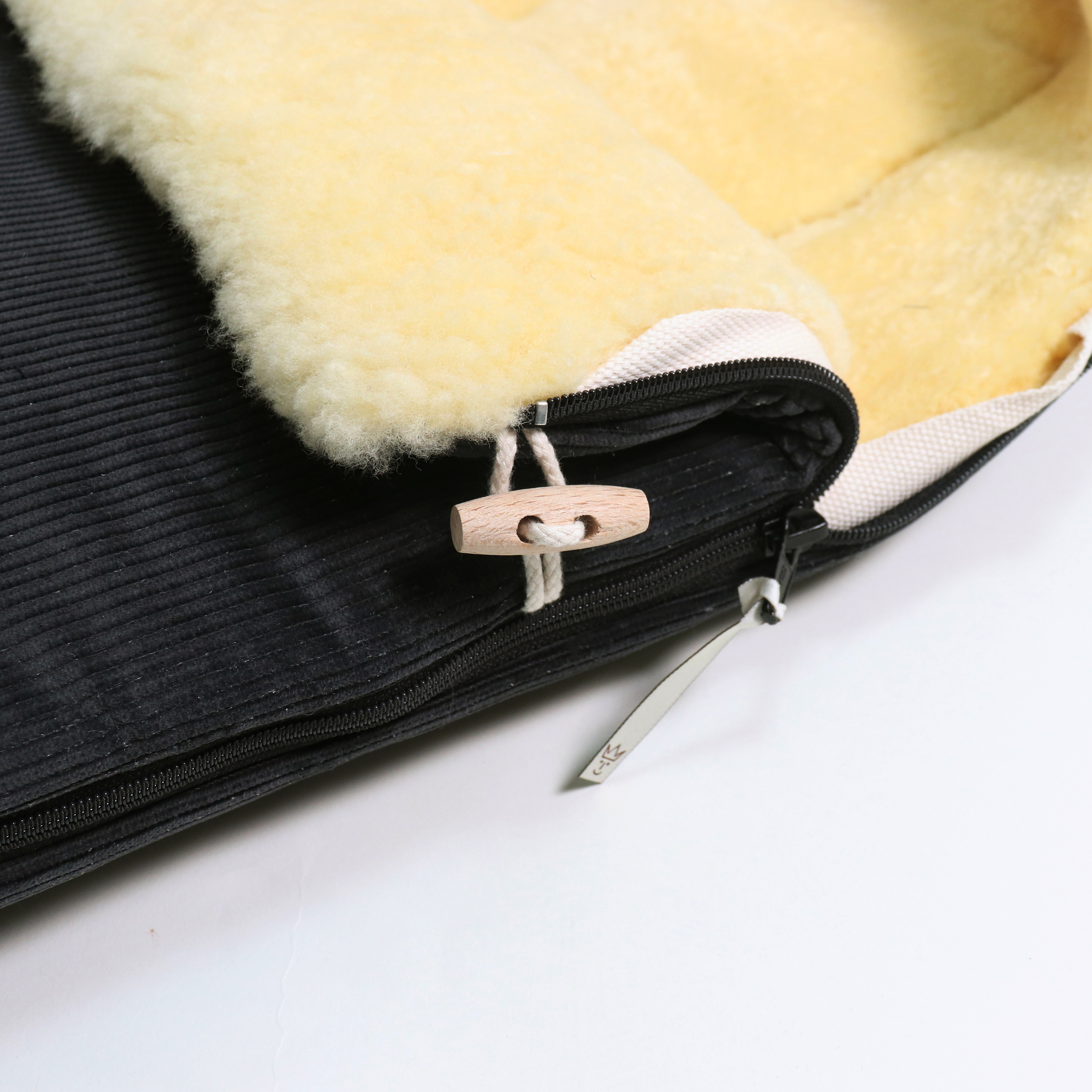 Detailaufnahme Reißverschluss und Holzknopf am FILIA CORD Babyschalen Fußsack mit Lammfell in der Farbe Black