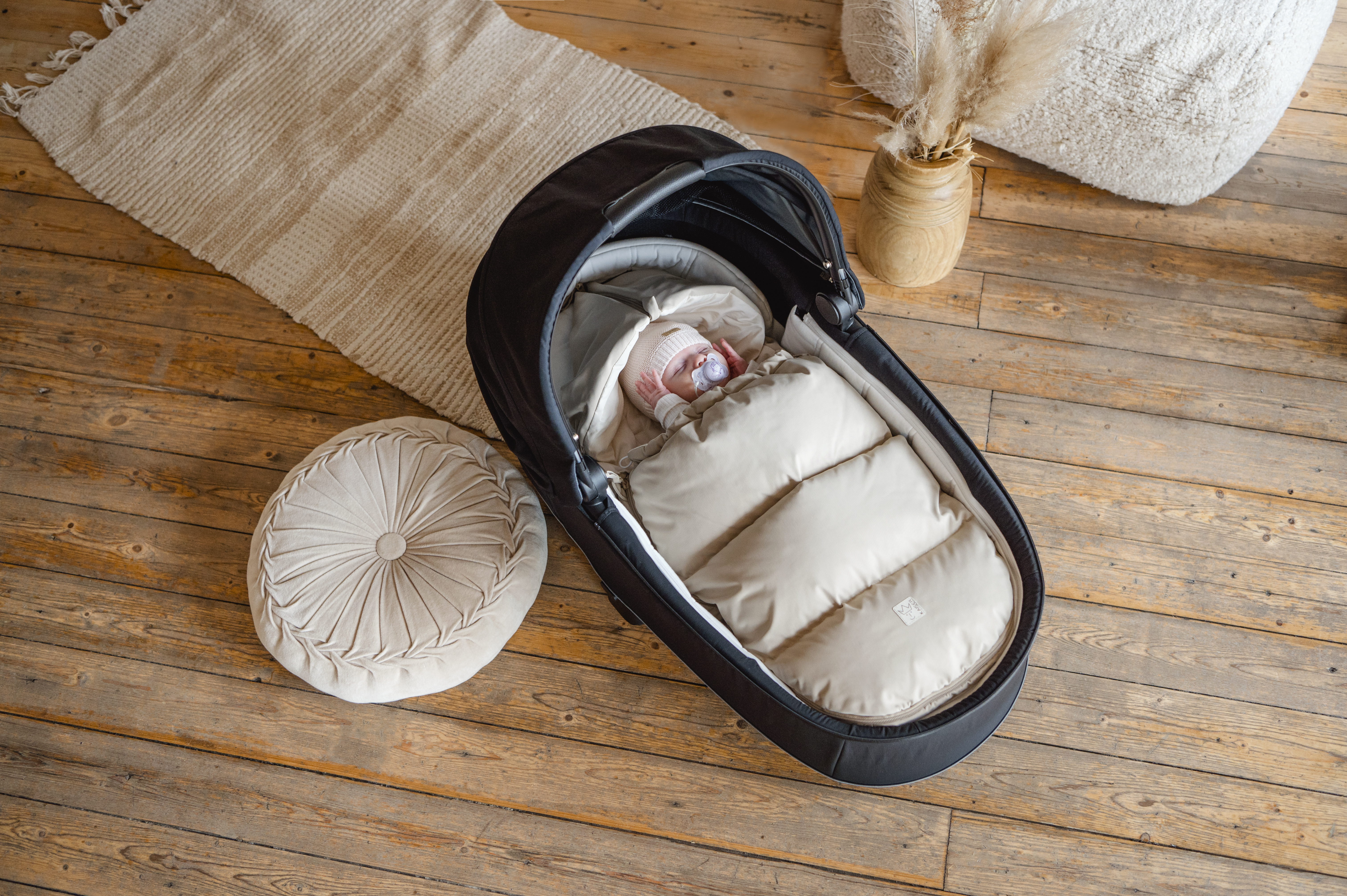 Baby liegt im LITTLE DOWNY Babyschalen-Fußsack in der Farbe sand in schwarzer Babyschale