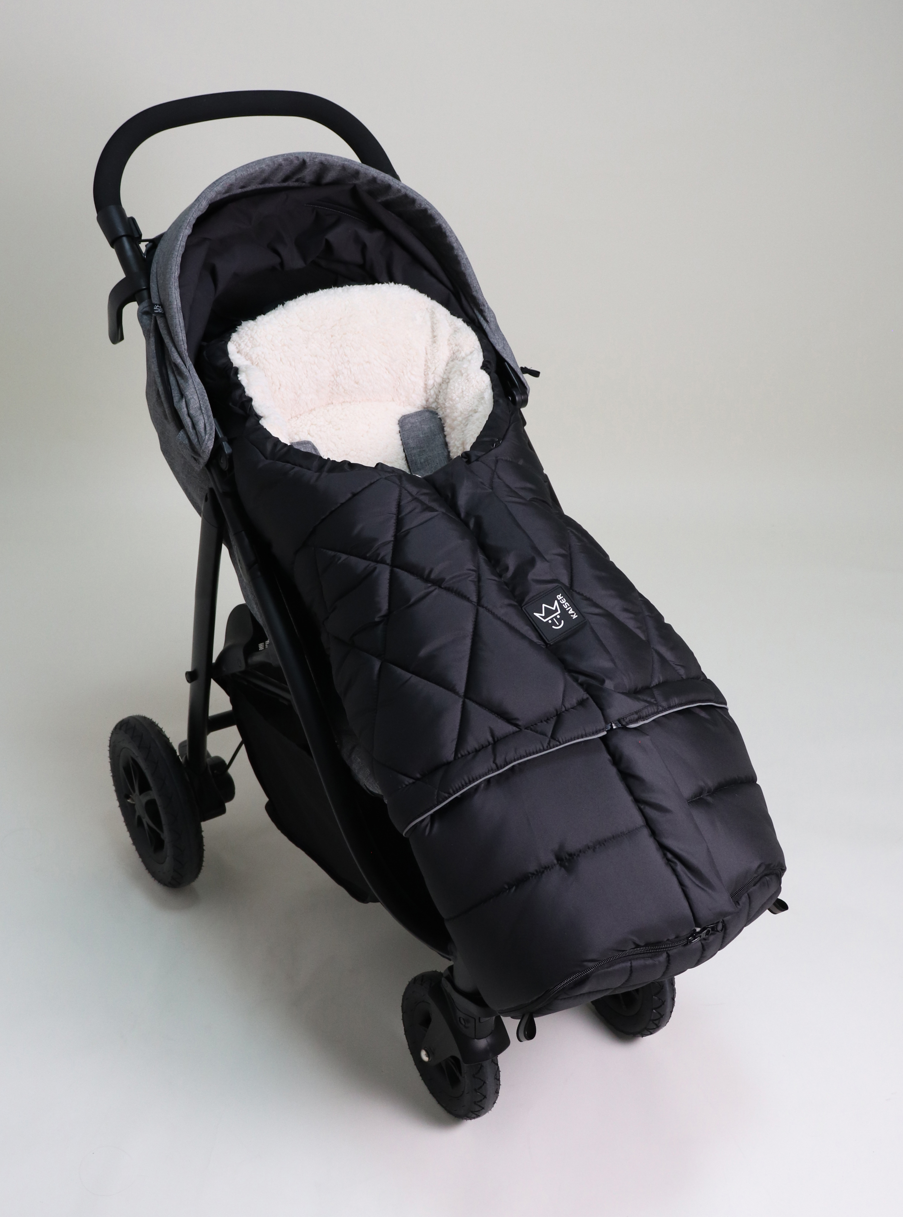 Fußsack mit einem Sherpa-Futter in der Farbe schwarz/creme ist in einem Kinderwagen eingesetzt