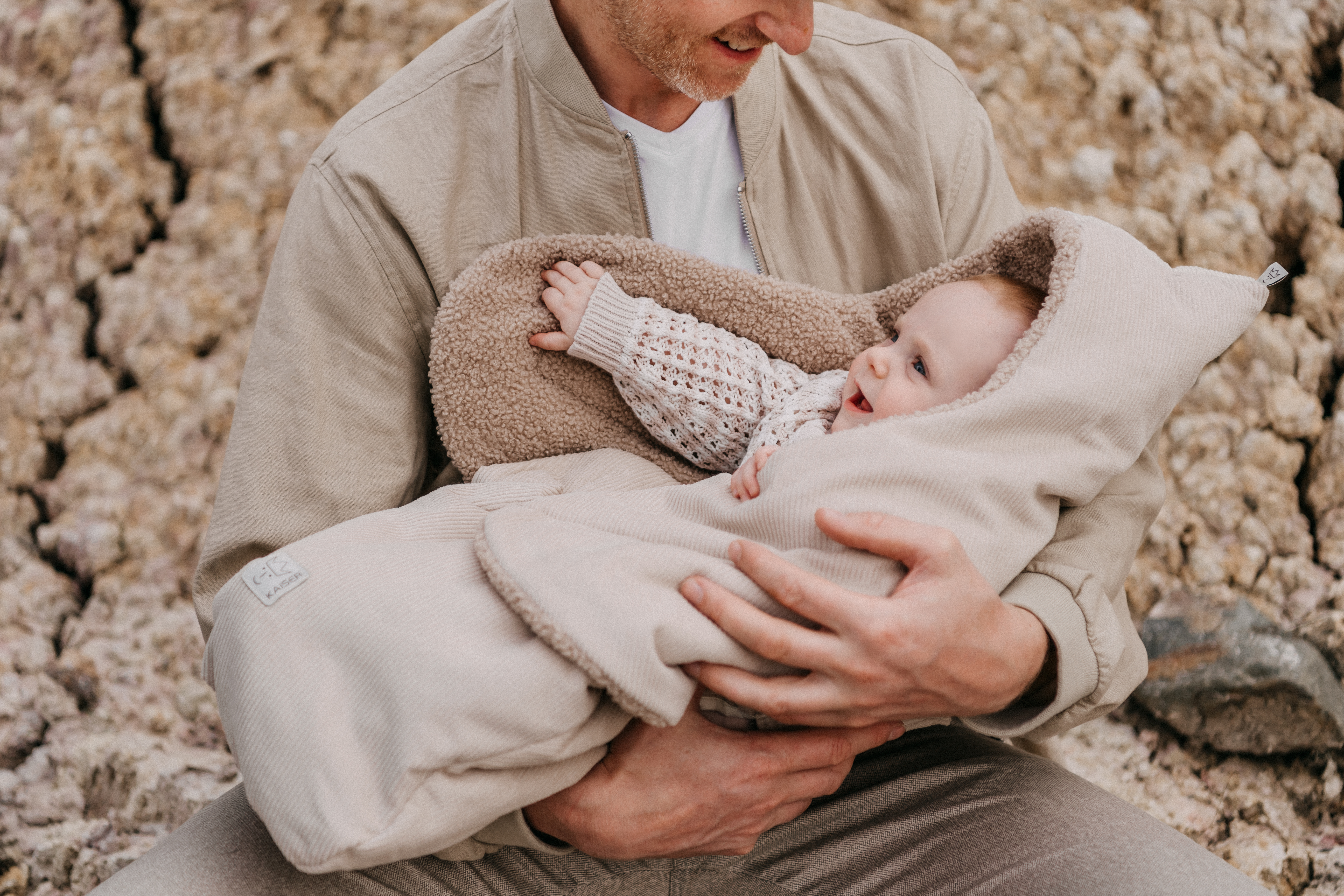 Baby in der CALLIE CORD Einschlagdecke sand shell – Outdoor Aufnahme mit Eltern