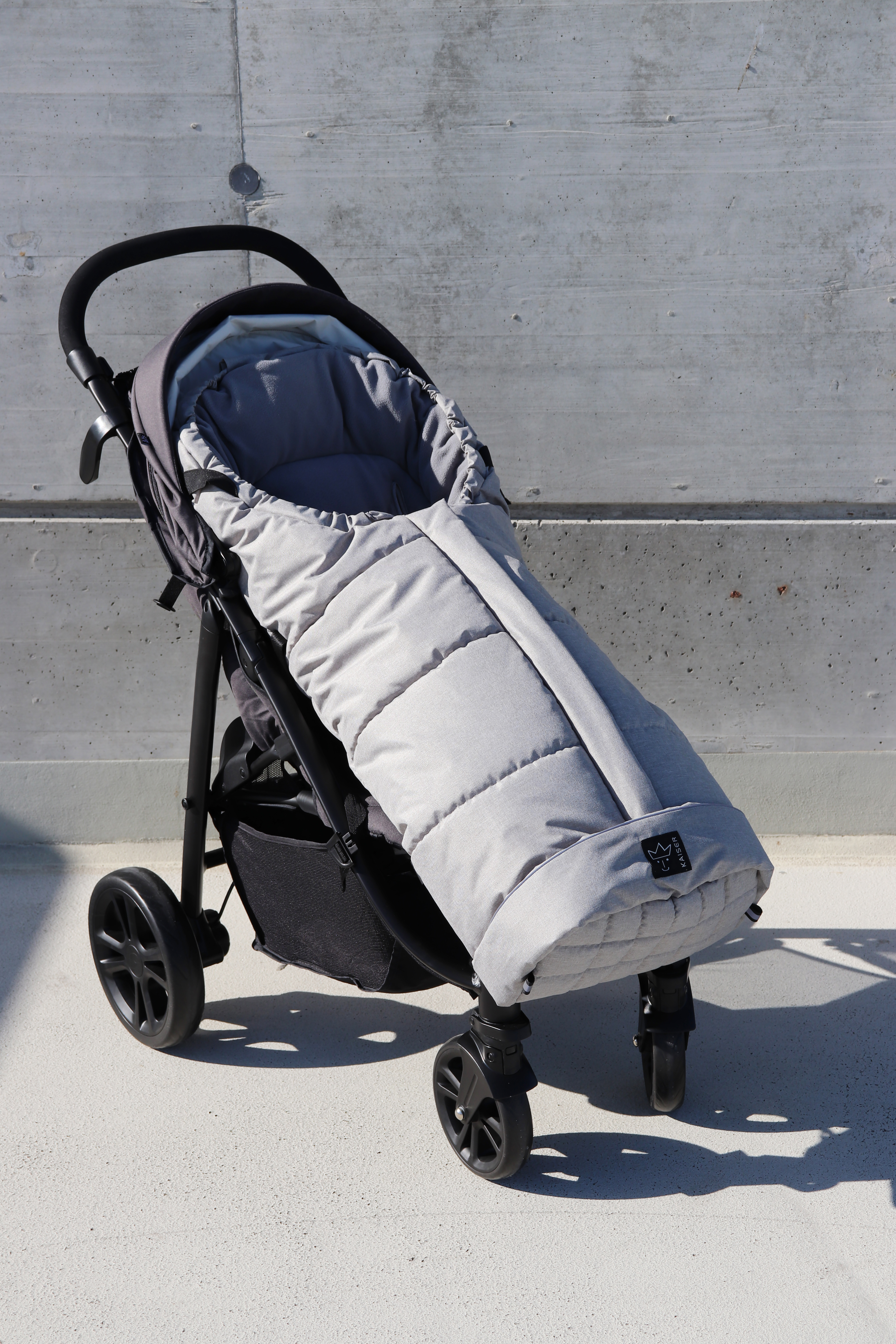 Thermofußsack in light grey melange mit schwarzem Logo ist in einem Kinderwagen eingesetzt